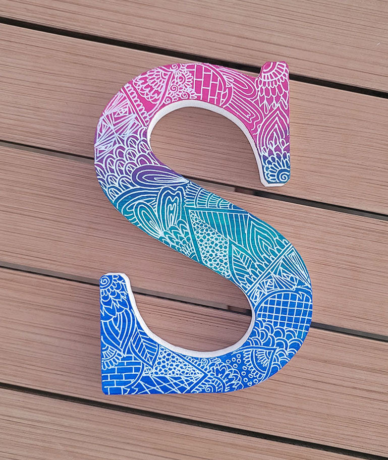 A gradient hand painted letter S (pink-green-blue) with doodles in white