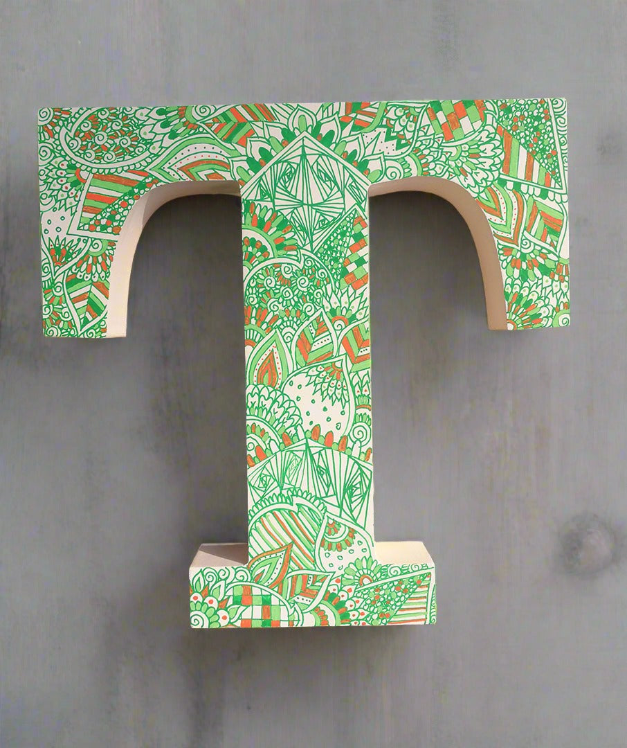 A white letter T with doodles drawn in green and colored in with light green , green and orange