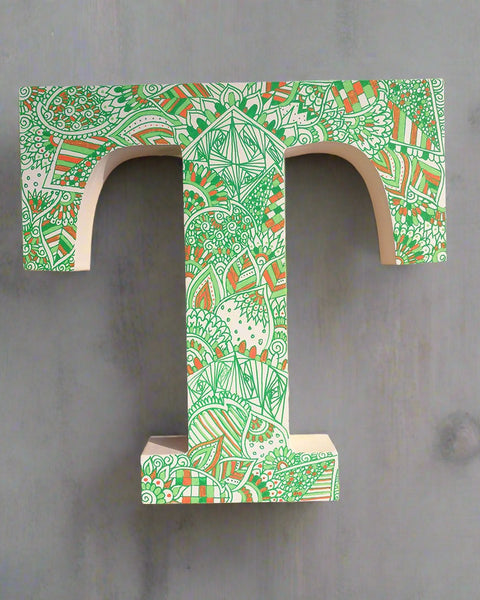 A white letter T with doodles drawn in green and colored in with light green , green and orange