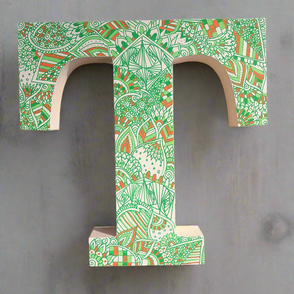 A white letter T with doodles drawn in green and colored in with light green , green and orange