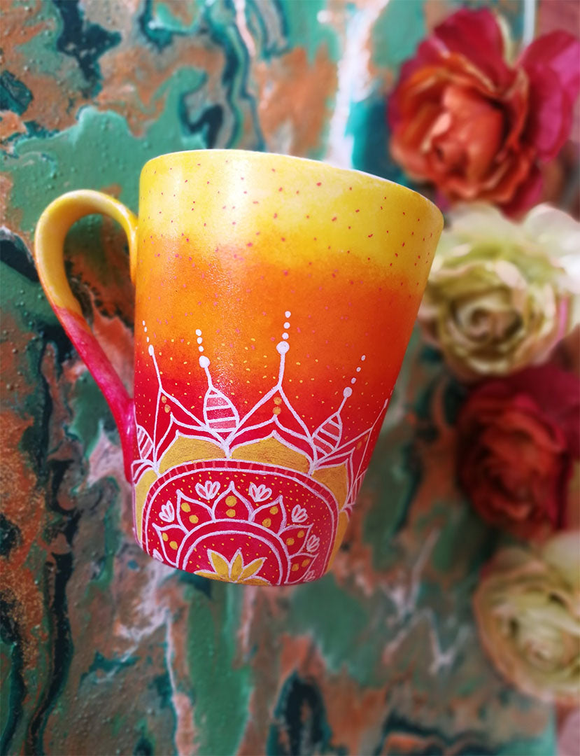 A Gradient hand painted mug from yellow to orange to red , with 1/2 a mandala drawn on the bottom