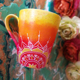 A Gradient hand painted mug from yellow to orange to red , with 1/2 a mandala drawn on the bottom