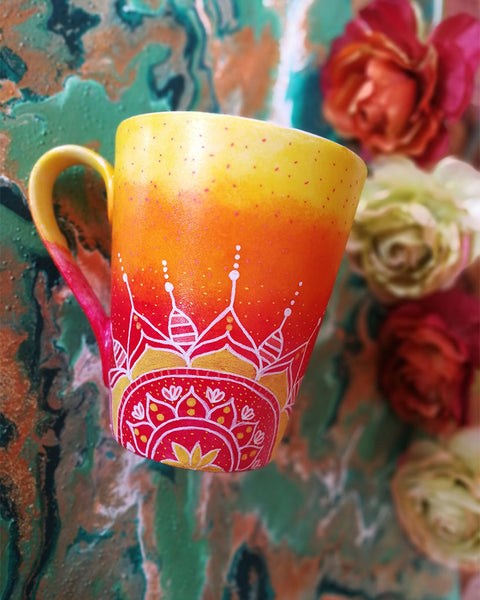 A Gradient hand painted mug from yellow to orange to red , with 1/2 a mandala drawn on the bottom