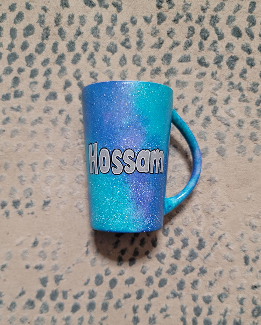 A blue Galaxy hand Painted mug with the name "Hossam"