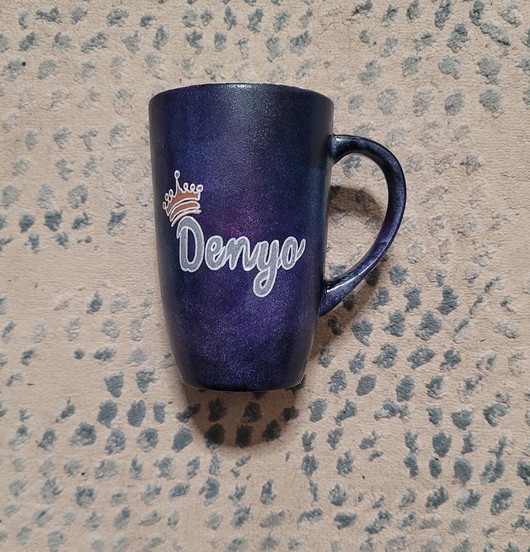 A dark sky hand painted mug with the name "Denyo" and a little crown above the letter D