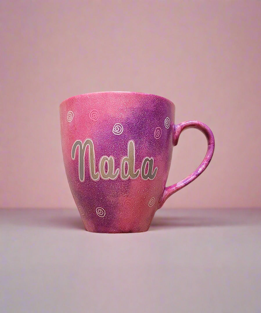 A Hand painted pink galaxy mug with the name "Nada" and small swirls all over the mug