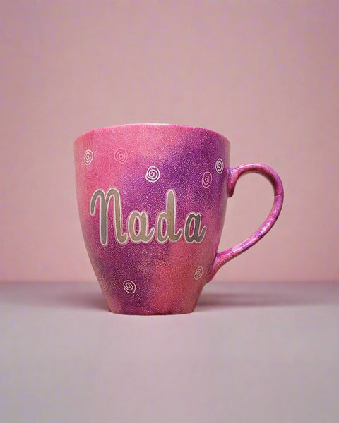 A Hand painted pink galaxy mug with the name "Nada" and small swirls all over the mug