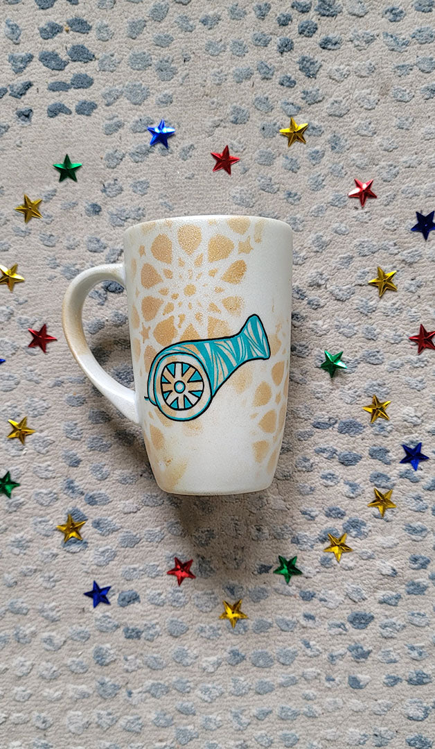 A Shimmery White with gold islamic patterns hand painted mug with a madfa3 painted in black and blue green patterns