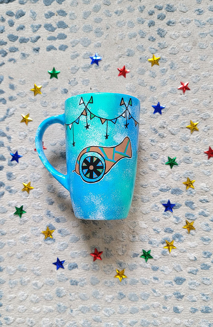 A Blue Green Hand painted mug with decorations hanging from the top all around the mug and a madfa3 painted in black brown, blue and green