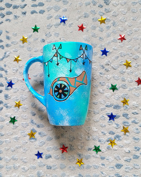 A Blue Green Hand painted mug with decorations hanging from the top all around the mug and a madfa3 painted in black brown, blue and green