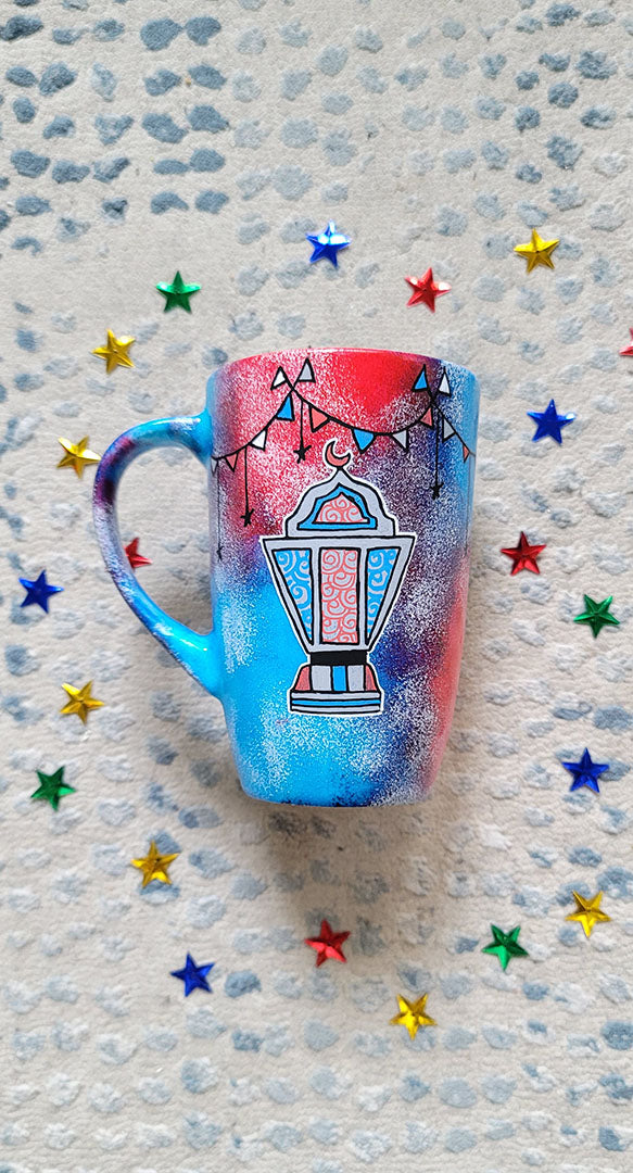 A Blue Red Hand painted mug with decorations hanging from the top all around the mug and a fanoos painted in black grey, blue and red