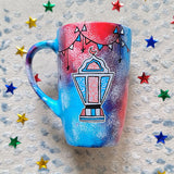 A Blue Red Hand painted mug with decorations hanging from the top all around the mug and a fanoos painted in black grey, blue and red