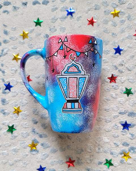 A Blue Red Hand painted mug with decorations hanging from the top all around the mug and a fanoos painted in black grey, blue and red