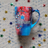 A Blue Red Hand painted mug with decorations hanging from the top all around the mug and a moon painted in black grey, blue and red and the name Kareem beside it