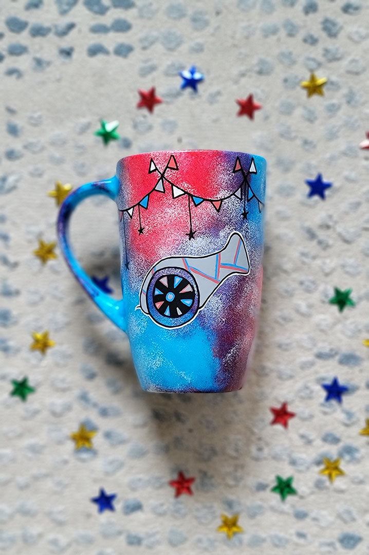 A Blue Red Hand painted mug with decorations hanging from the top all around the mug and a Madfa3 painted in black grey, blue and red