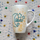 A Shimmery White with gold islamic patterns hand painted mug with a moon painted in black and blue green and the name Abir beside it