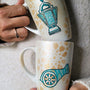 2 hand painted mugs in white shimmery color and faded gold islamic patterns one with a fanoos and the other with a madfa3