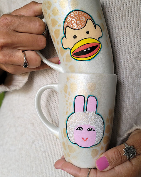 2 shimmery white hand painted mugs with a faded geometric pattern in gold, one with bogi and the other with tamtam