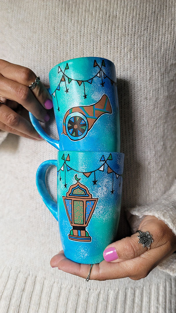 2 hand painted mugs in blue green color with decorations all around the top and one has a fanoos and the other a madfa3