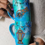 2 hand painted mugs in blue green color with decorations all around the top and one has a fanoos and the other a madfa3