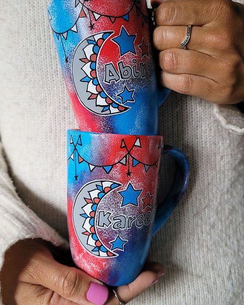 2 hand painted mugs in blue green color with decorations all around the top and one has a moon a name abir the other has a moon and name kareem