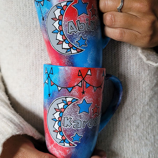 2 hand painted mugs in blue green color with decorations all around the top and one has a moon a name abir the other has a moon and name kareem