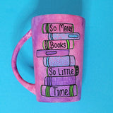 A Pink hand painted mug with books on top of each other and words written in between making the sentence