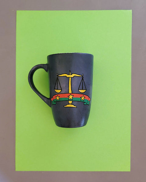 A greyish hand apinted mug with the Egyptian prosecution logo on it