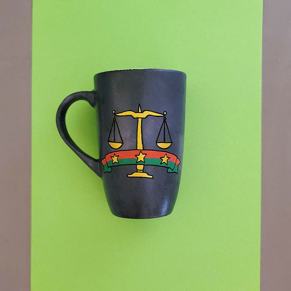 A greyish hand apinted mug with the Egyptian prosecution logo on it