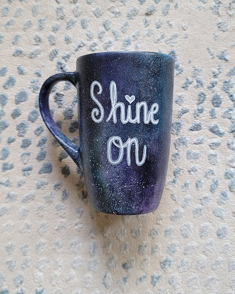 A Black galaxy hand painted mug with the words "Shine on"