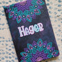 A Black galaxy hand painted noteboo with 2 half mandalas one on top and one at the bottom with the name "Hagar" in the center