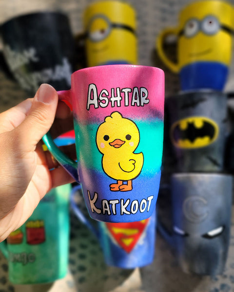 A gradient Hand painted mug (pink- green and blue) with the word "Ashtar" on top the the duck painted in the center then the word "Katkoot" below it