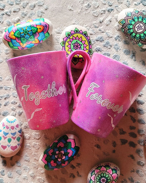 2 hand-painted Pink Galaxy Mugs , one has the word together in silver and white outline and the other has the word forever in silver and white outline