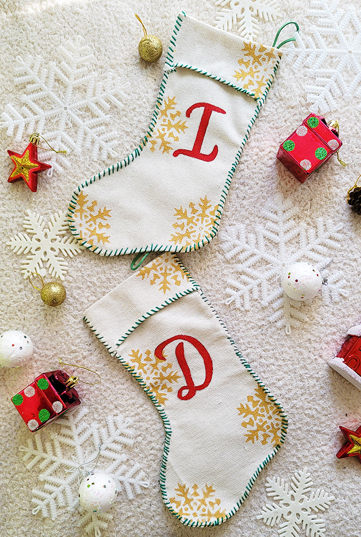 A Picture of two stockings on top of each other ne woht the letter I in red and the other with the Letter D in red, sewn in green thread all around with gold snowflakes in the background