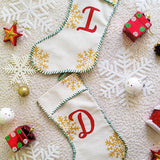 A Picture of two stockings on top of each other ne woht the letter I in red and the other with the Letter D in red, sewn in green thread all around with gold snowflakes in the background