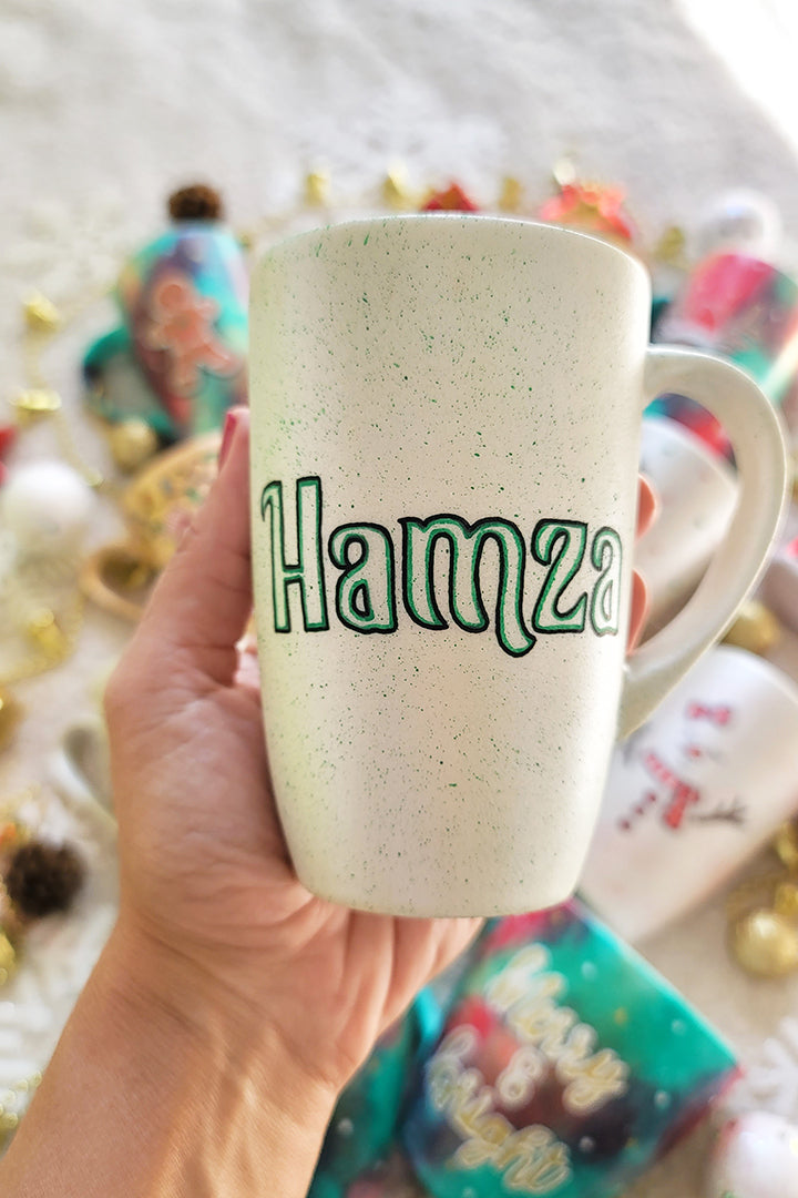 A pearl white hand painted mug with the name "Hamza"