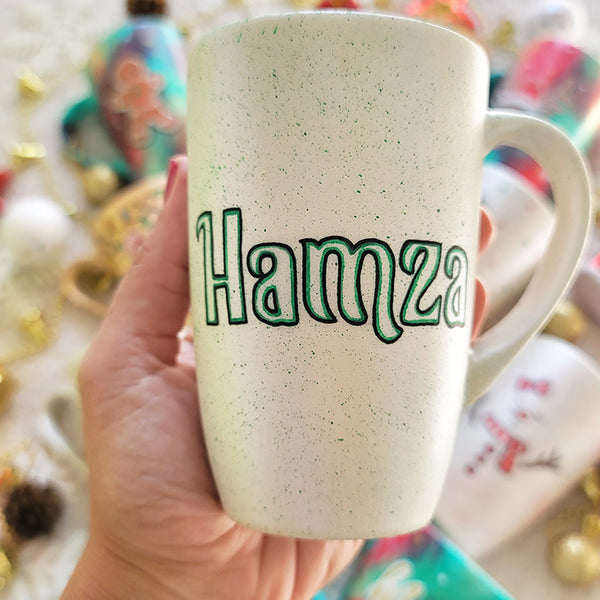 A pearl white hand painted mug with the name "Hamza"