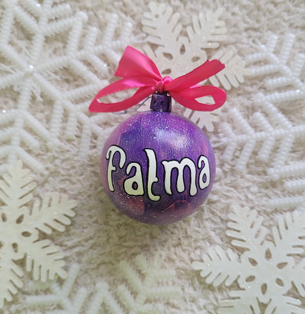 A Purple hand painted ornament with the name "Fatma" written in white outlined with black