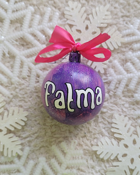 A Purple hand painted ornament with the name "Fatma" written in white outlined with black