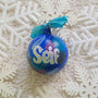 A Colorful hand painted ornament with blue background and colors of blue, black dark purple and silver scattered all over with white dots and the name "seif" written in silver outlined with white