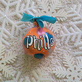 A Colorful hand painted ornament with Orange background and colors of orange, blue, pink and silver scattered all over with white dots and the name 