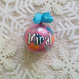 A Colorful hand painted ornament with pastel pink background and colors of pastel pink, teal orange and silver scattered all over with white dots and the name 