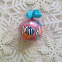 A Colorful hand painted ornament with pastel pink background and colors of pastel pink, teal orange and silver scattered all over with white dots and the name "Miral" written in white outlined with black