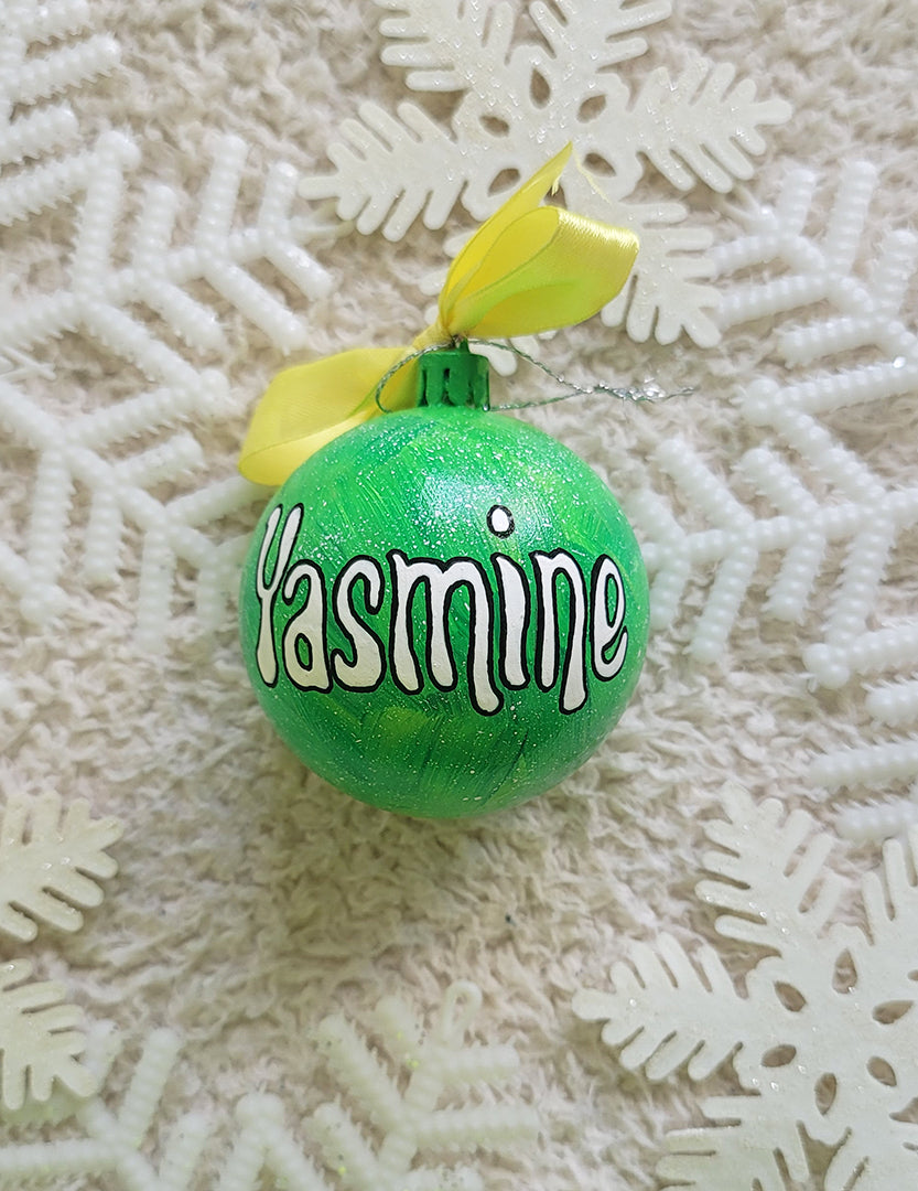 A lime green galaxy hand painted ornament with the name "yasmine" written in white outlined with black