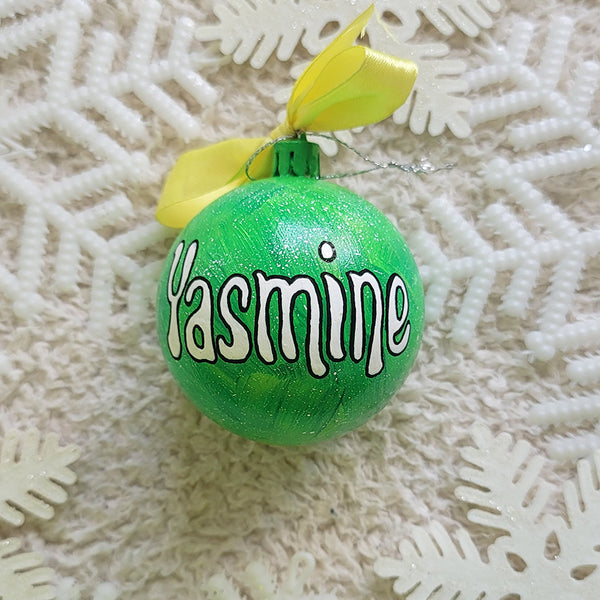 A lime green galaxy hand painted ornament with the name "yasmine" written in white outlined with black