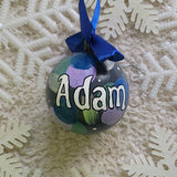 A Colorful hand painted ornament with Grey background and colors of lilac, blue, green and silver scattered all over with white dots and the name 