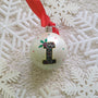 A Pearl white hand painted ball ornament with the letter "I" drawn filled with black doodles and colored with green and red, outlined with gold and green  and red dots scattered all over the ball with gold stars