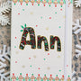 A Pearl white notebook with the letters "ANN" written filled with doodles in black and colored in green and red. then hz patterns drawn all through the bottom of the mug. with green and red dots, and gold stars scattered all over