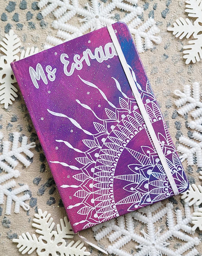 A Pink Galaxy hand painted notebook with a quarter mandala drawn from the corner and the name "Ms. Esraa" written on top