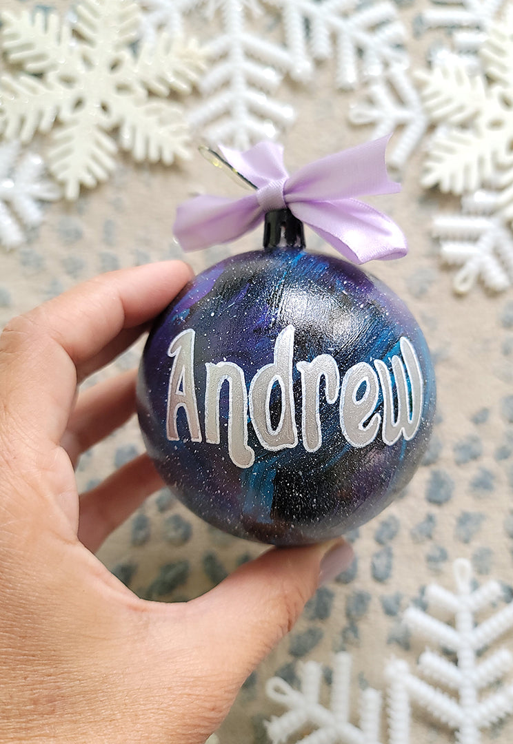 A Black galaxy hand painted ball ornament with the name "Andrew" in silver